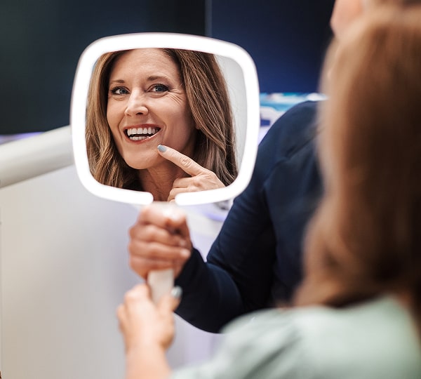Transform Your Smile with Natural Cosmetic Dentistry in Miami Shores. A woman is smiling and looking into hand mirror