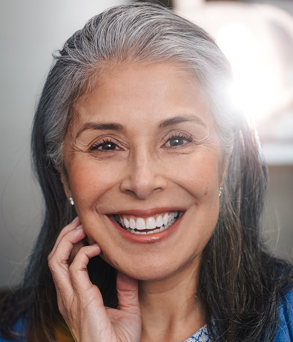Rebuild Your Smile with Durable Crowns and Bridges. A woman is smiling with a hand near her face