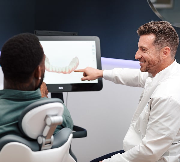 All-on-4 Implants: Full Smile Restoration Made Easy. Blu Dental dentist showing digital model of a jaw to a happy patient and smiling