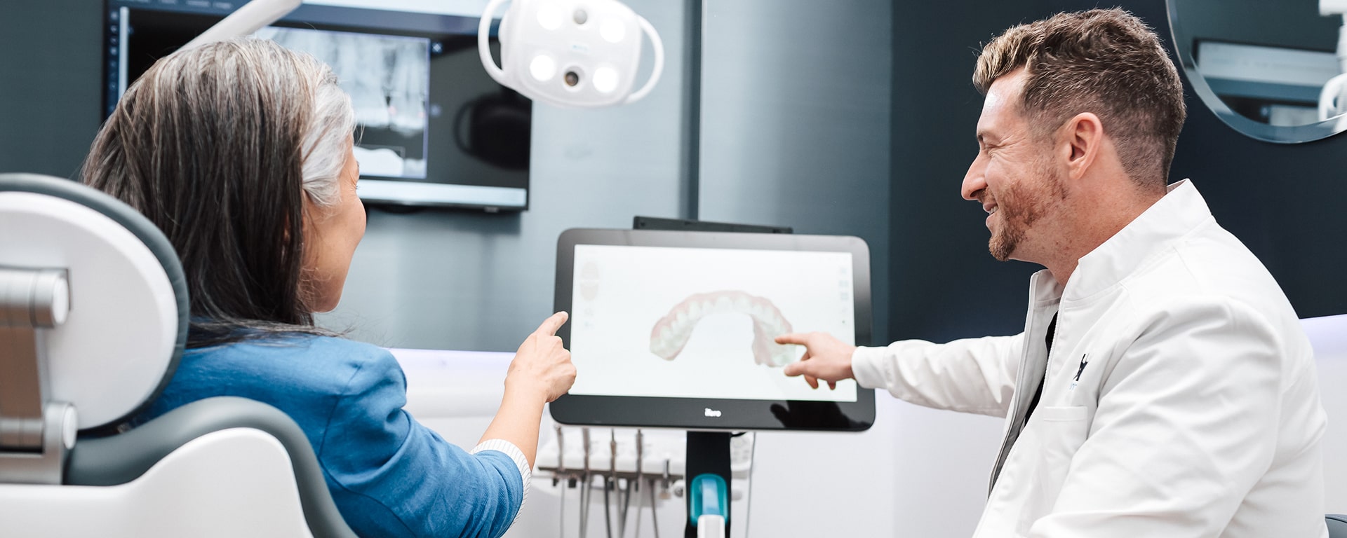 What to Expect with Implants at Blu Dental. Dentist discussing dental implants with his client and smiling