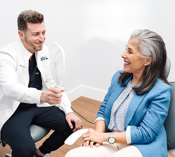 Eat & Speak Confidently with Implant-Supported Dentures. Dentist with a happy patient in a chair - both smiling