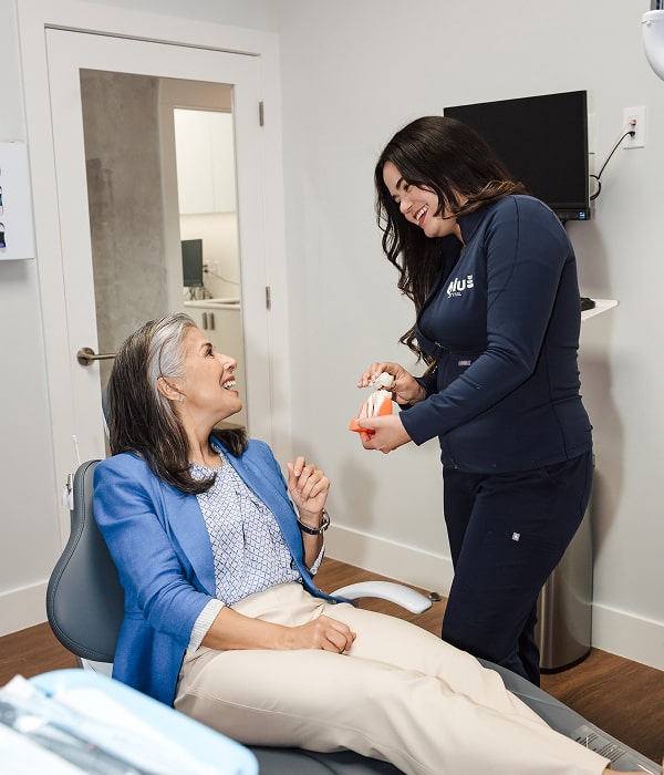 Enjoy a Stronger Bite and Confident Smile with Dental Implants. A woman in a dental chair is joyfully smiling with her dentist
