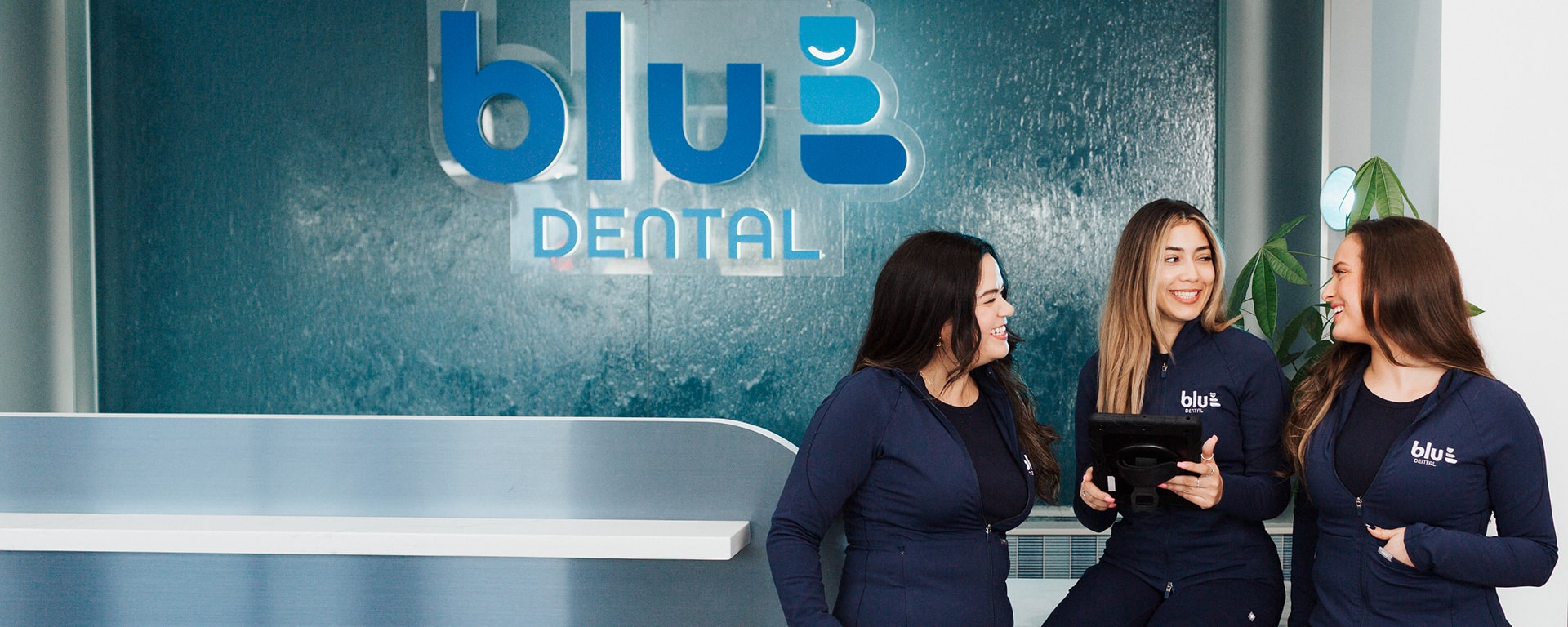 Blu Dental team is smiling at front desk near Blu Dental logo