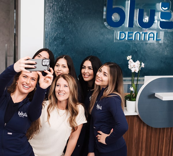 Blu Dental team is smiling while makin group selfie at front desk near Blu Dental logo