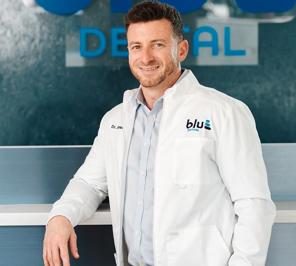 Dr. Jared is joyfully smiling with Blu Dental logo behind