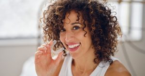 Woman holding an Invisalign tray and smiling