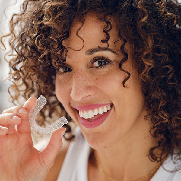 A Curly woman smiling while holding Invisalign